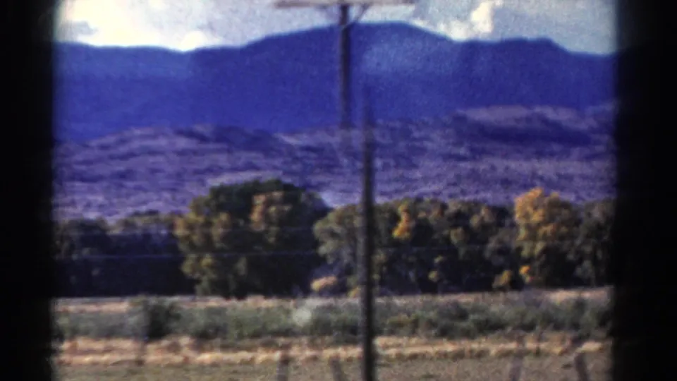 Colorado landscape from a moving vehicle with mountain ridge, wooded foreground, field, and a utility pole crossing the view.