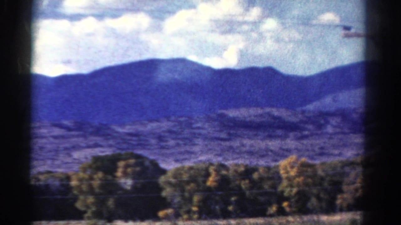 1967 Colorado home-movie view of distant mountains, low trees, power lines, and blurred foreground framing from a road-trip perspective.