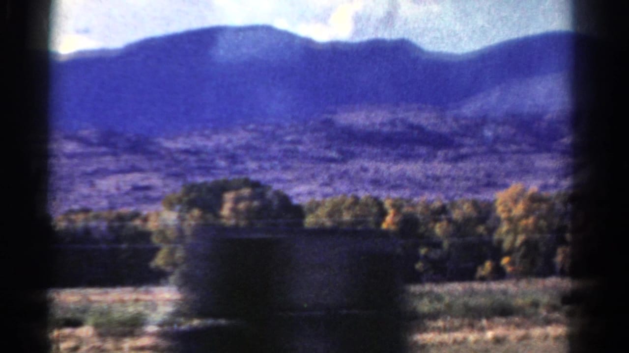 Mountain ridge, open foothills, roadside trees, and a dark vertical foreground obstruction.