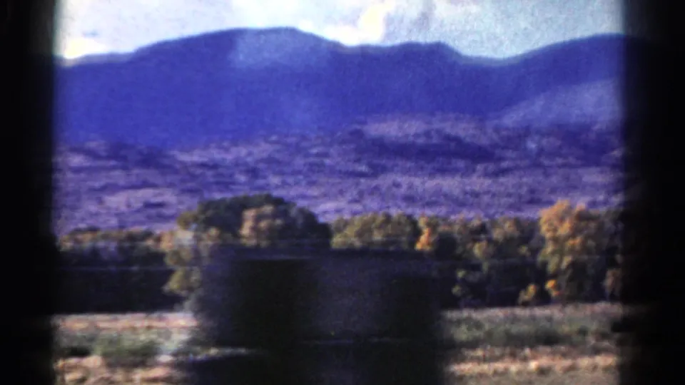 1967 Colorado landscape with a broad mountain ridge, open foothills, trees, and a dark foreground obstruction from the moving viewpoint.
