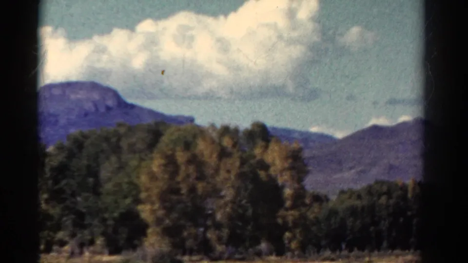 1967 Colorado road-trip frame showing clouds above a mountain slope with autumn-toned trees in the foreground.