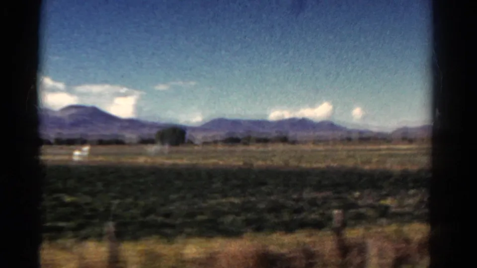 Final 1967 Colorado road-view frame with open land, distant mountains, small trees, clouds, and visible 8mm frame borders.