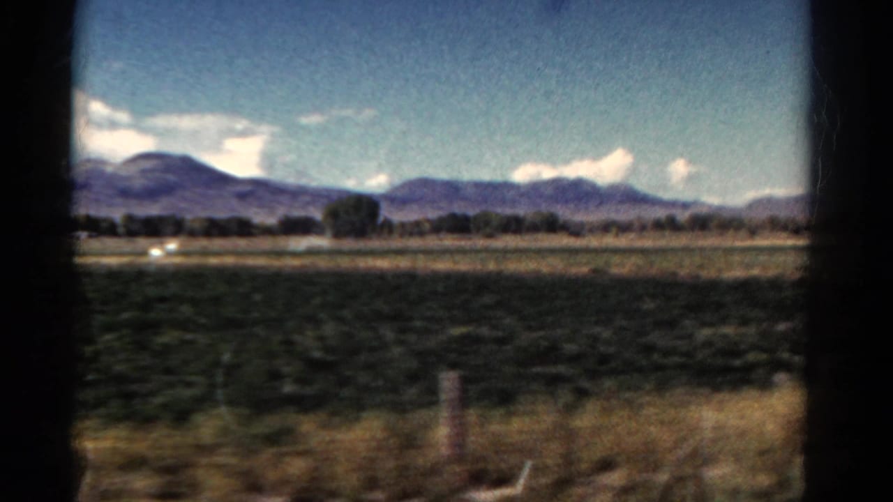 Farmland and distant mountains seen from a moving vehicle through 8mm frame edges.