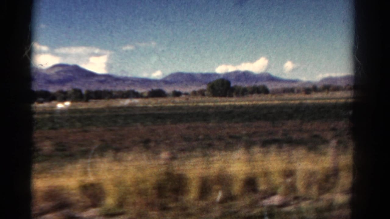 Distant mountains, fields, trees, and sky framed by a vehicle window.