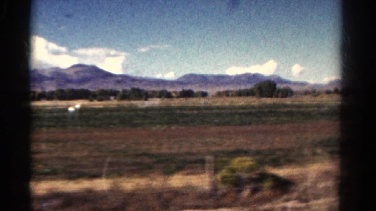 1967 Colorado train-window view over grassy fields toward distant mountains under a bright sky, with blurred foreground showing motion.
