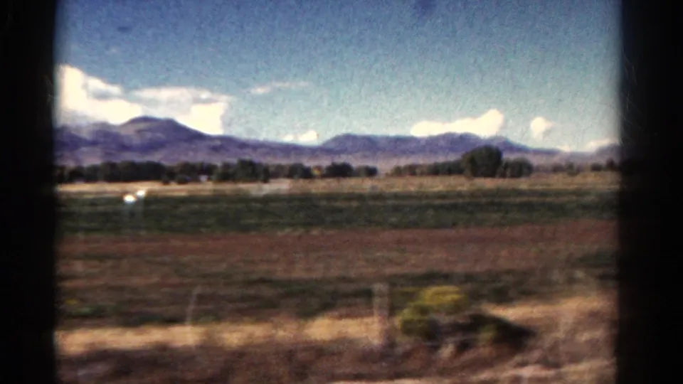 1967 Colorado train-window view over grassy fields toward distant mountains under a bright sky, with blurred foreground showing motion.