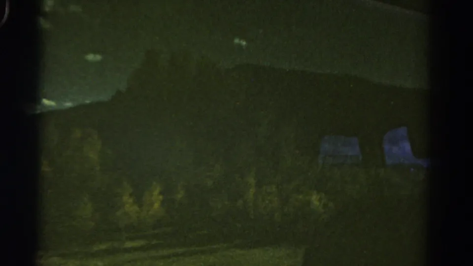 1967 Colorado 8mm frame showing a dim mountain ridge and roadside vegetation seen through dark vehicle-window framing.