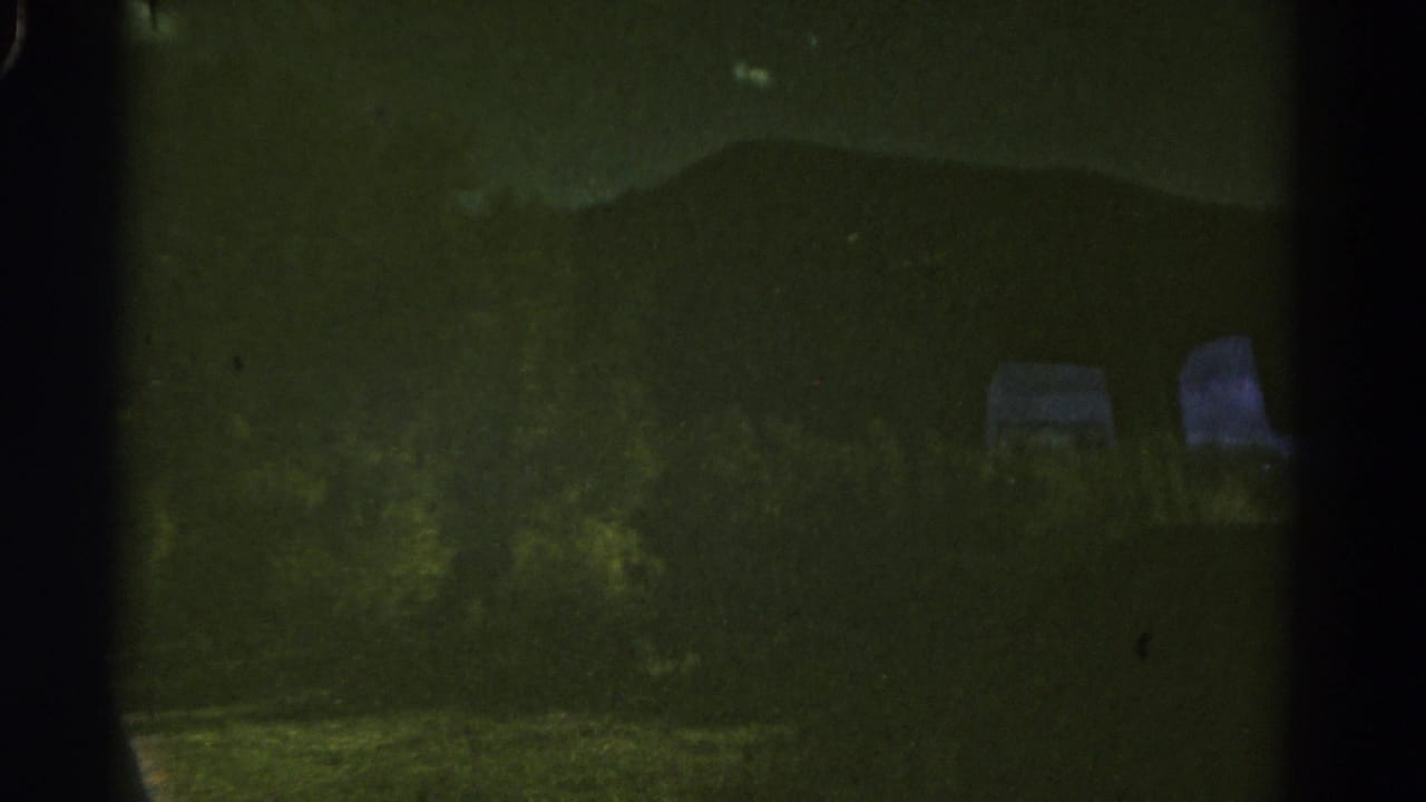 Dim mountain landscape with roadside brush and two pale shapes near the right edge.