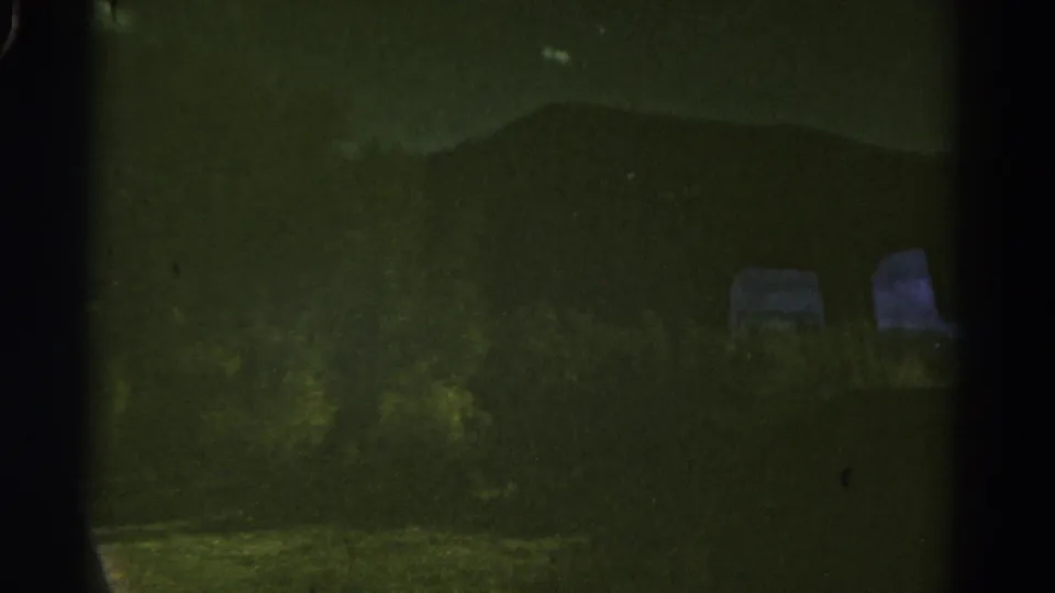 1967 Colorado roadside scene from a moving car, with dark mountains, brush, and faint pale objects in low light.