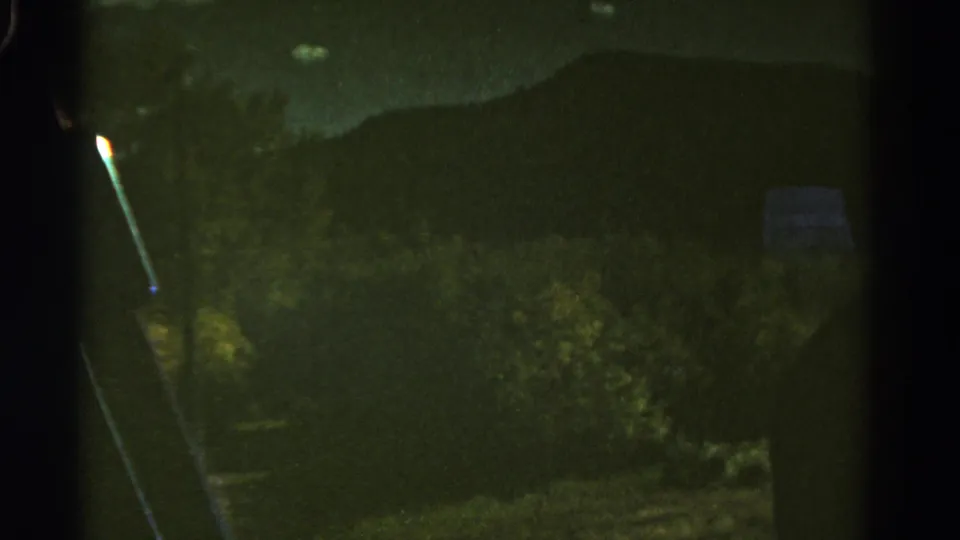 1967 Colorado 8mm frame with vehicle framing, roadside brush, distant mountains, and a faint pale roadside object.