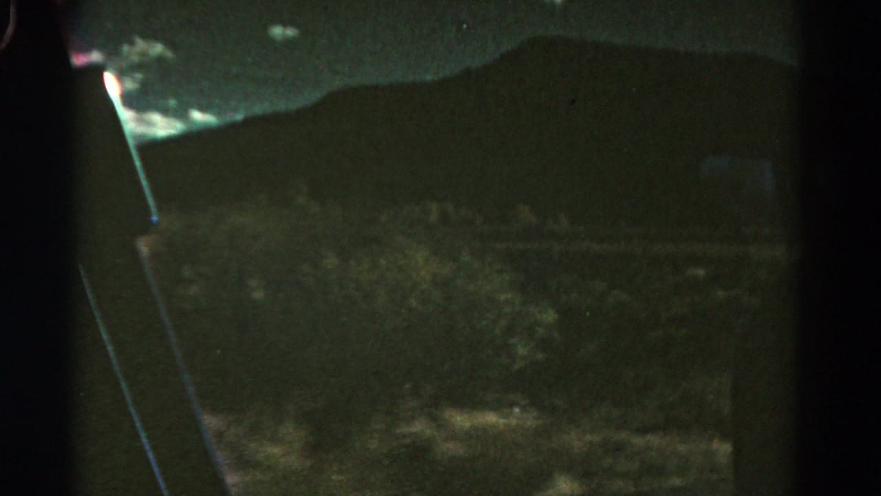 Dark hillside and cloudy sky seen through a vehicle window at night.