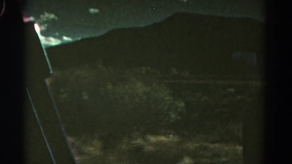 1967 Colorado home-movie frame showing a dark hillside, cloudy sky, and vehicle-window edges during nighttime travel.