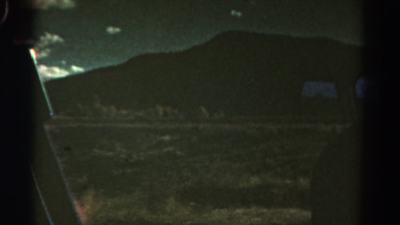 1967 Colorado 8mm frame with a dark hillside beyond a vehicle window, faint clouds, and low-light roadside terrain.