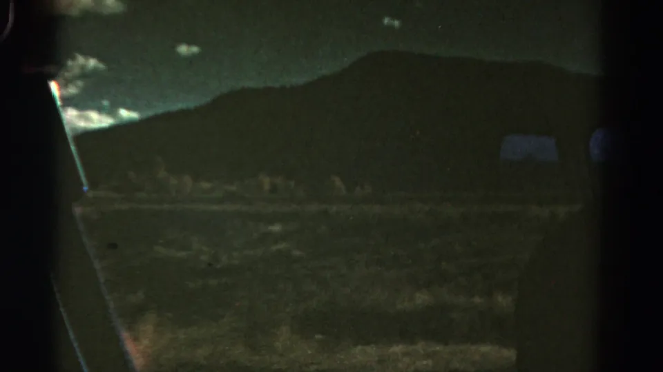 1967 Colorado 8mm frame with a dark hillside beyond a vehicle window, faint clouds, and low-light roadside terrain.