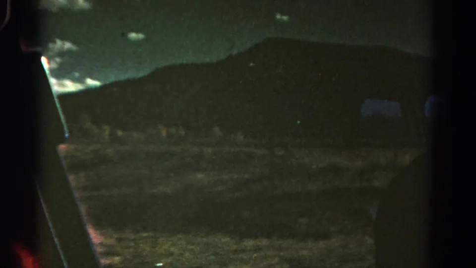 1967 Colorado travel footage frame showing a dim hillside, vehicle-window framing, and faint roadside detail in low light.