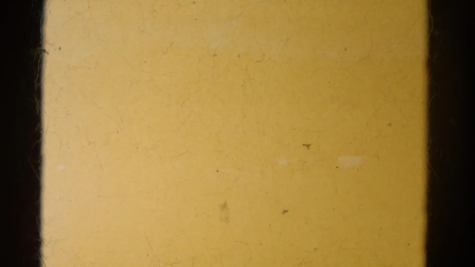 A yellowish exposed film area fills the frame, bordered by dark 8mm gate edges before the trailer park view appears.