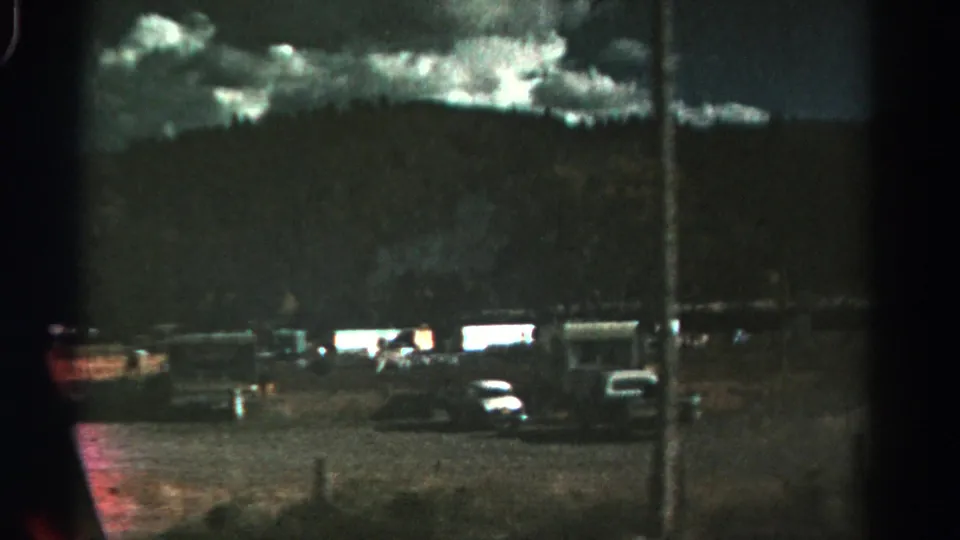 Dark 1967 Colorado 8mm frame with parked cars, a truck, mobile homes, a utility pole, hills, and cloudy sky.