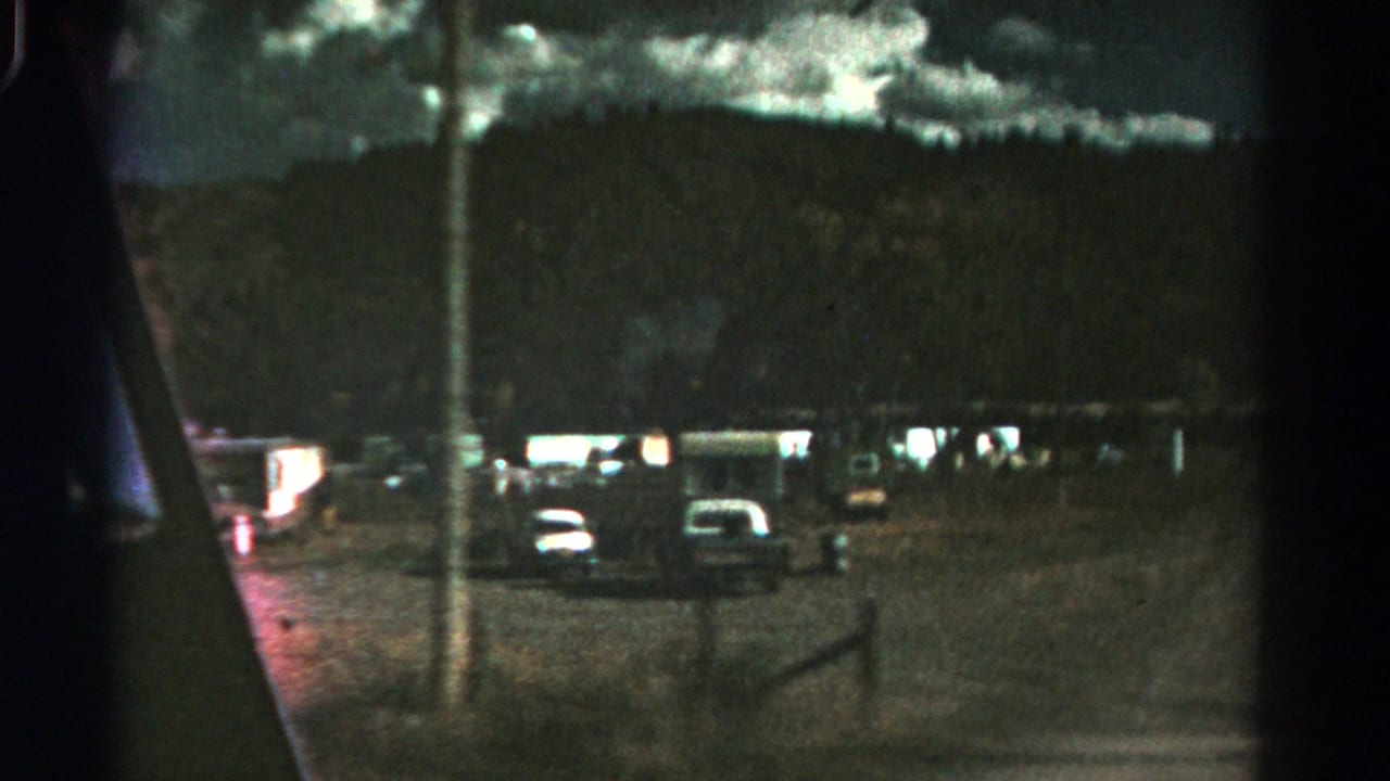 1967 Colorado 8mm frame showing parked cars in a gravel area beneath a dark mountain ridge and cloudy sky.