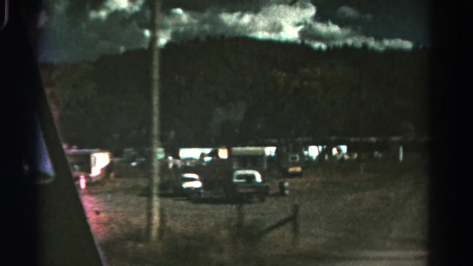1967 Colorado 8mm frame showing parked cars in a gravel area beneath a dark mountain ridge and cloudy sky.