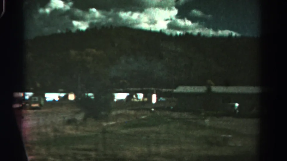 1967 Colorado 8mm frame showing a dim campground or roadside lot with trailers, parked vehicles, and a mountain backdrop.