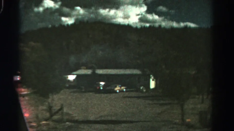 1967 Colorado 8mm frame showing a dim rural building, parked cars, hillside, and clouds at night.