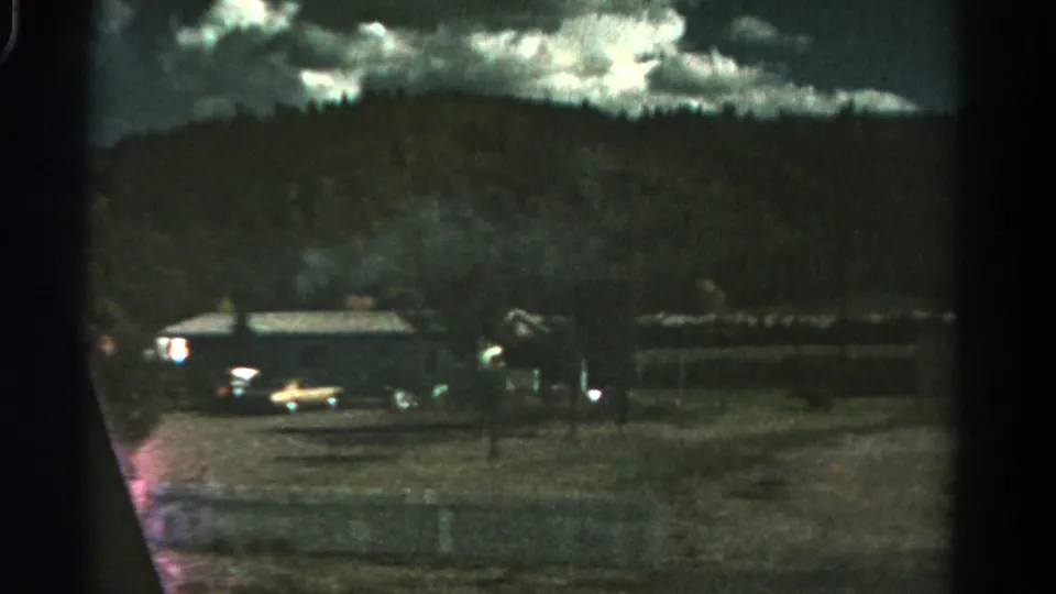1967 Colorado home-movie frame of parked cars near a rural building and fence line at night.