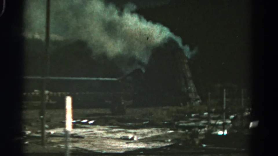 1967 Colorado home-movie frame with smoke, dim yard lighting, posts, and a rural structure at night.