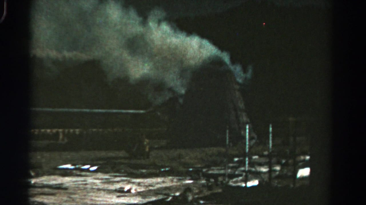1967 Colorado 8mm frame showing a smoky industrial exterior with dark structures, vertical posts, and reflective ground below.