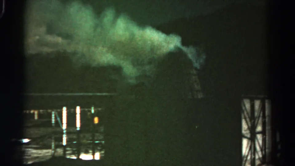 1967 Colorado 8mm frame showing green-tinted smoke above an industrial yard, with metal posts and light reflections in the foreground.