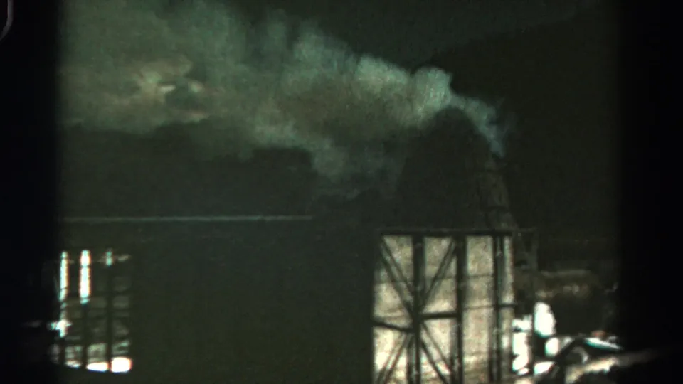 1967 Colorado 8mm frame showing smoke over a dark factory area and a cross-braced metal framework in the foreground.