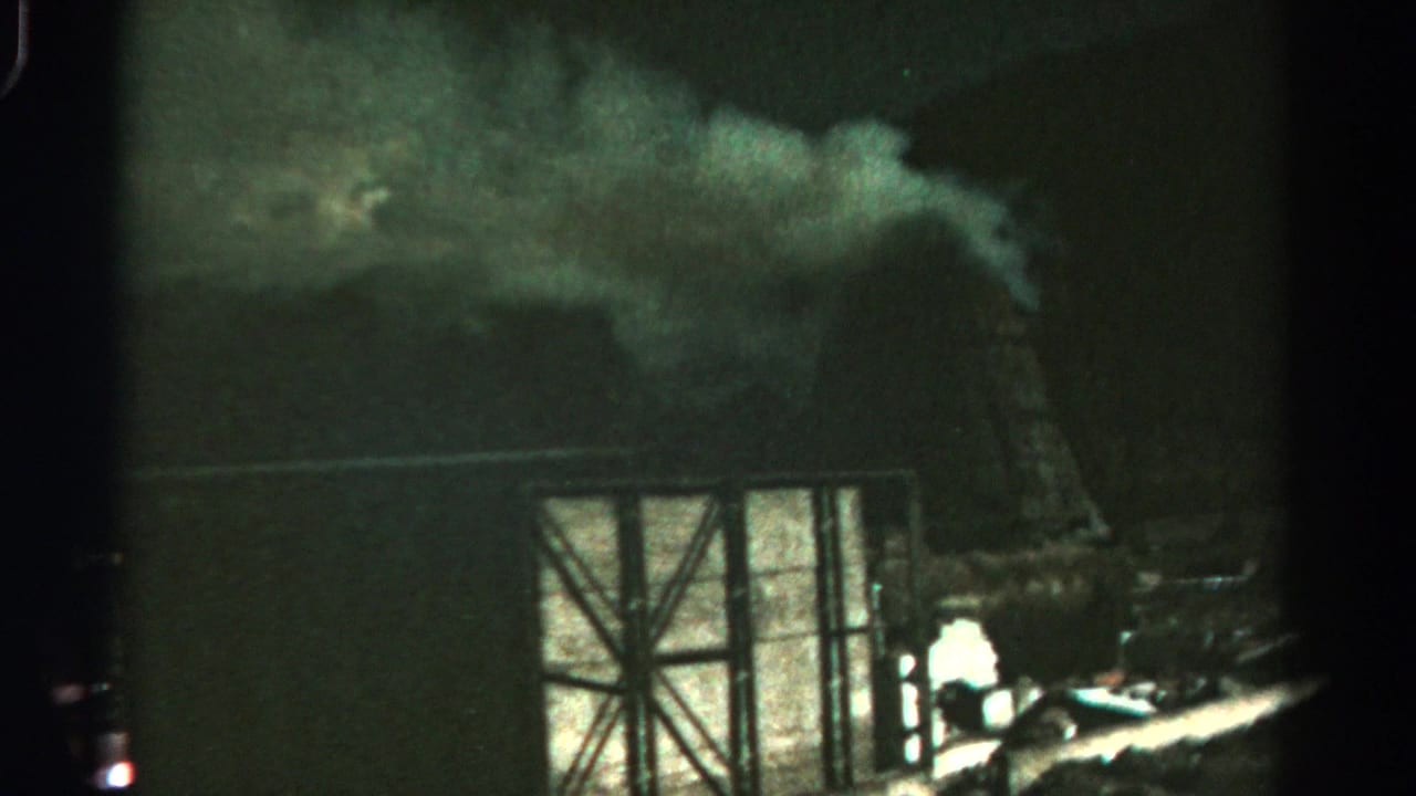 1967 Colorado 8mm frame showing a nighttime smoke plume above wooden framing, with firelight near debris in the foreground.