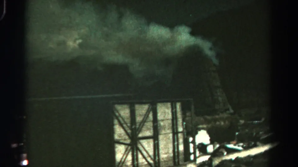 1967 Colorado 8mm frame showing a nighttime smoke plume above wooden framing, with firelight near debris in the foreground.