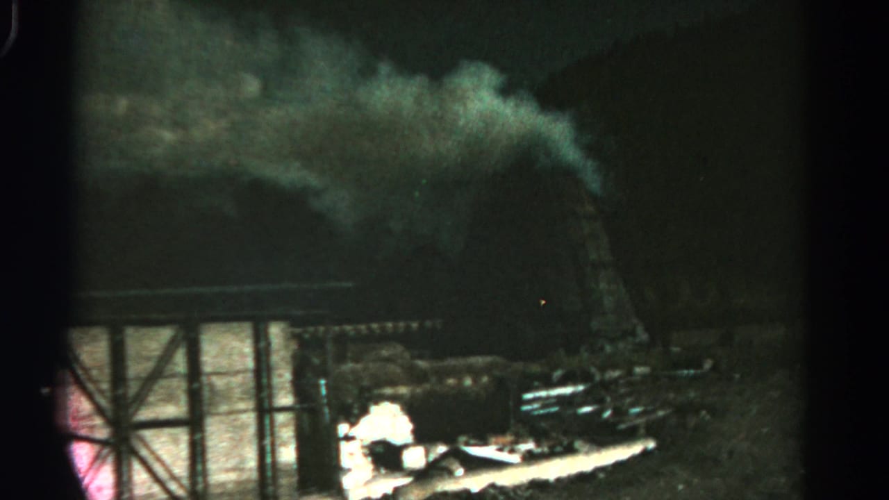 Smoke billows over a dark structure with bright flames or firelight near the lower edge.