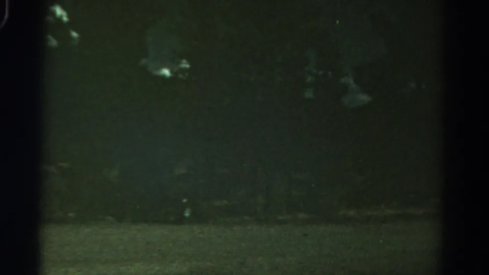 Underexposed 1967 Colorado 8mm frame with faint smoke or reflected light visible above a mostly dark outdoor scene.