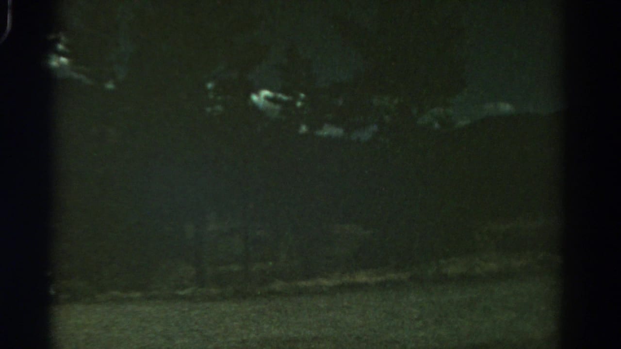1967 Colorado home-movie frame showing dim clouds against a dark sky above a barely visible landscape.