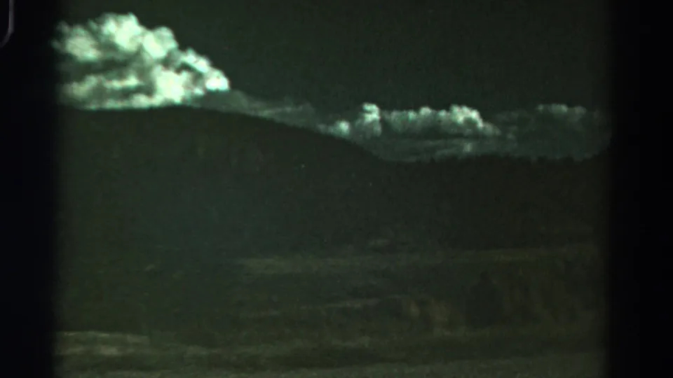 1967 Colorado home-movie frame showing a bright cloud bank above a dark, sloping horizon and dim ground.