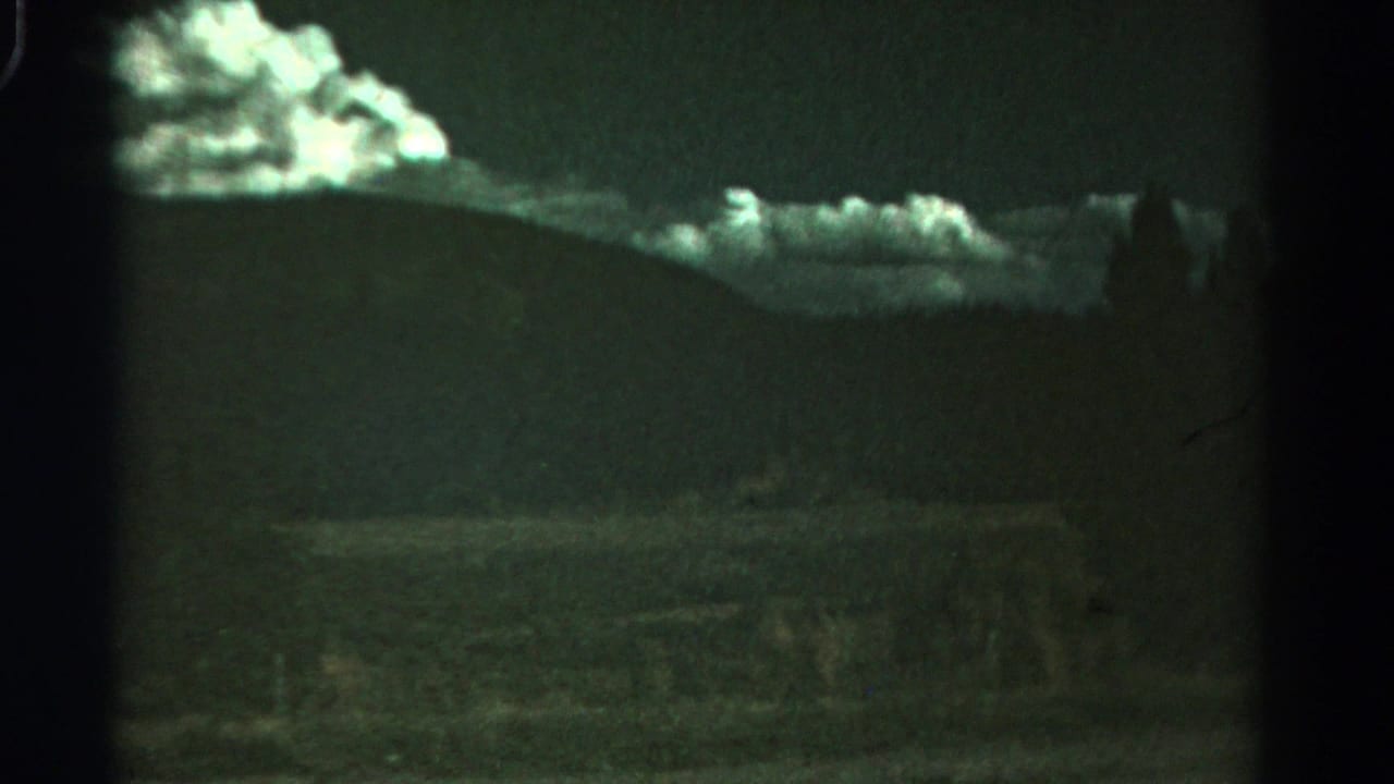 1967 Colorado 8mm frame with dark hill silhouettes, glowing clouds, and a dim rural foreground seen through film gate edges.
