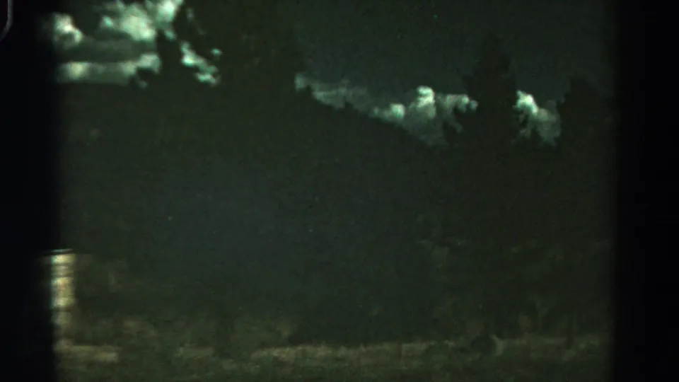 1967 Colorado 8mm frame with cloud highlights, a low hill line, roadside brush, and pronounced grain in a dark night view.