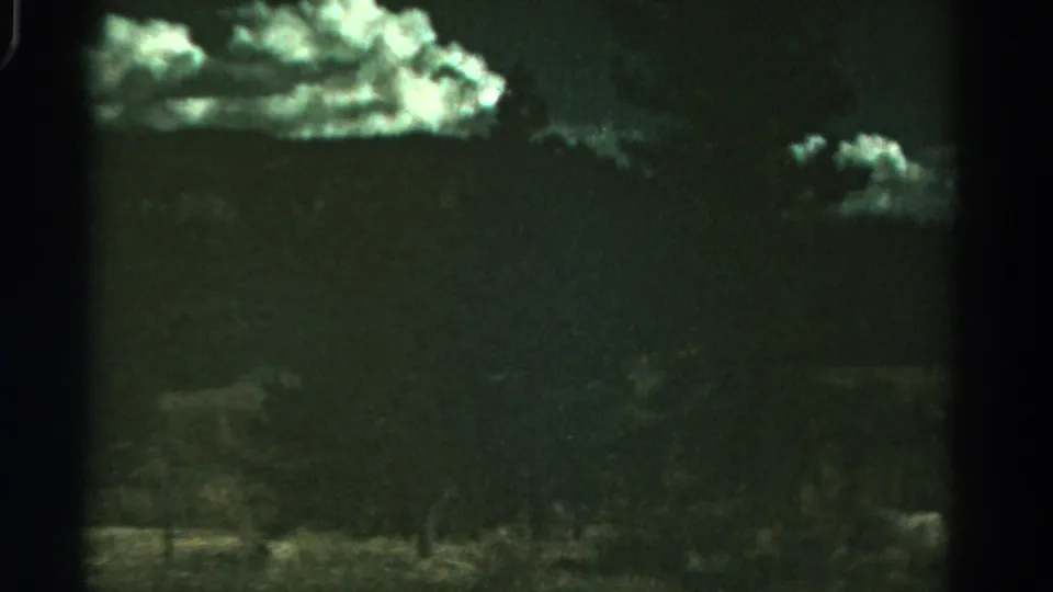 1967 Colorado 8mm frame with white clouds against a dark green sky, low hill forms, and shadowed roadside vegetation.