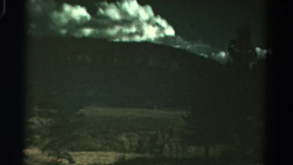 Soft 8mm frame from Colorado showing a dark hillside, bright upper clouds, and indistinct brush or grassland in the foreground.