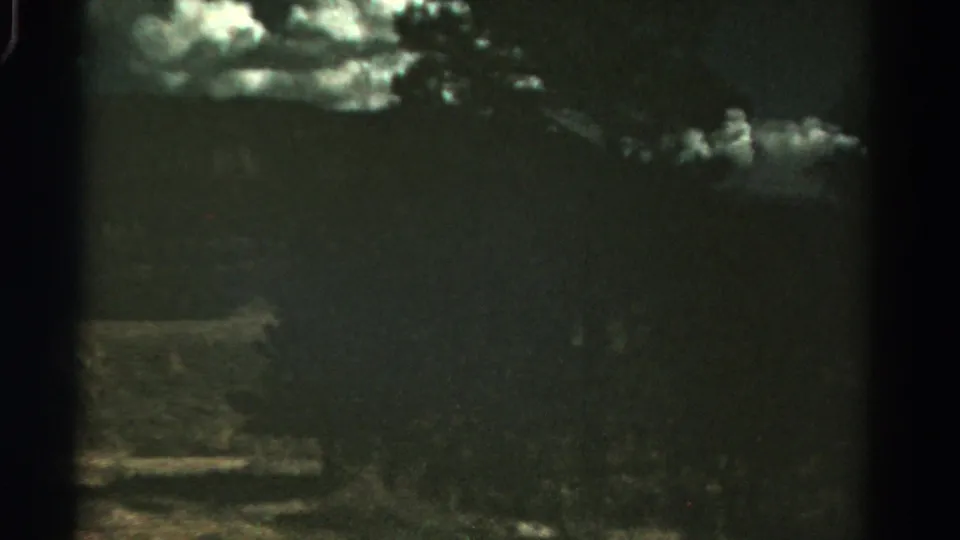 End frame of a 1967 Colorado 8mm pan, with shadowed mountain terrain, bright clouds, trees, and faint open foreground land.