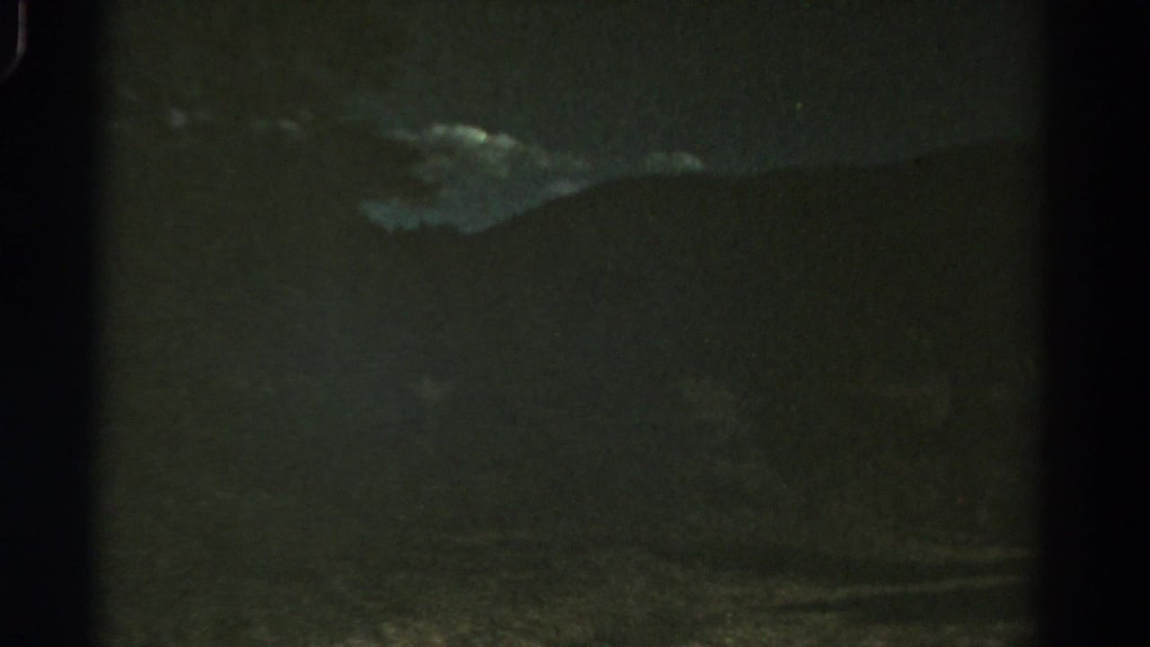 1967 Colorado 8mm frame looking from a moving vehicle toward shadowed hills, trees, and low cloud.