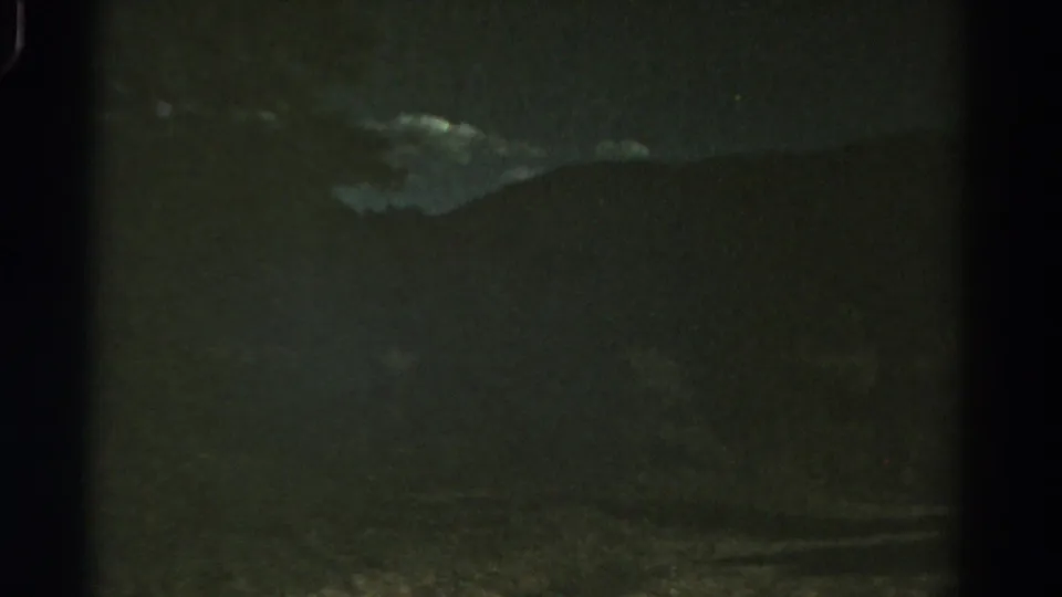 1967 Colorado 8mm frame looking from a moving vehicle toward shadowed hills, trees, and low cloud.