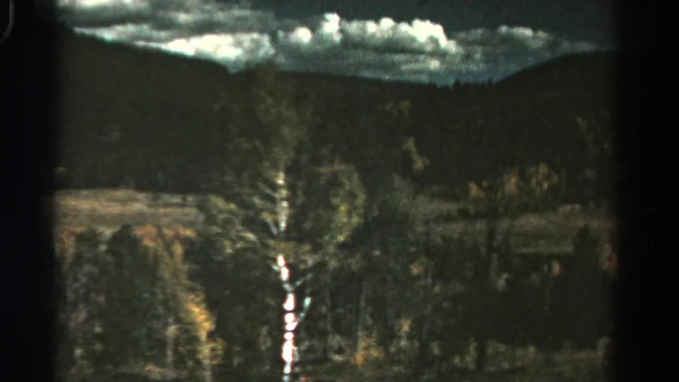 Moving 8mm view in Colorado with a dark window divider, wooded hillside, and bright cloud band above.