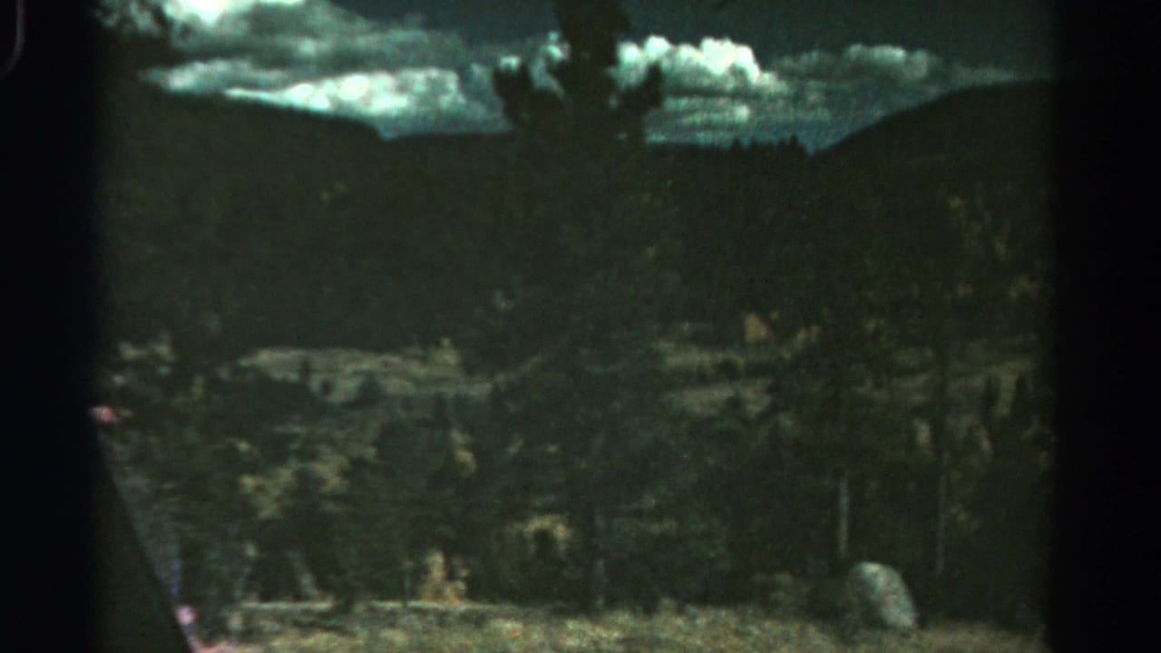 1967 Colorado landscape frame with a forested slope, distant ridge, pale clouds, and visible 8mm gate edges.