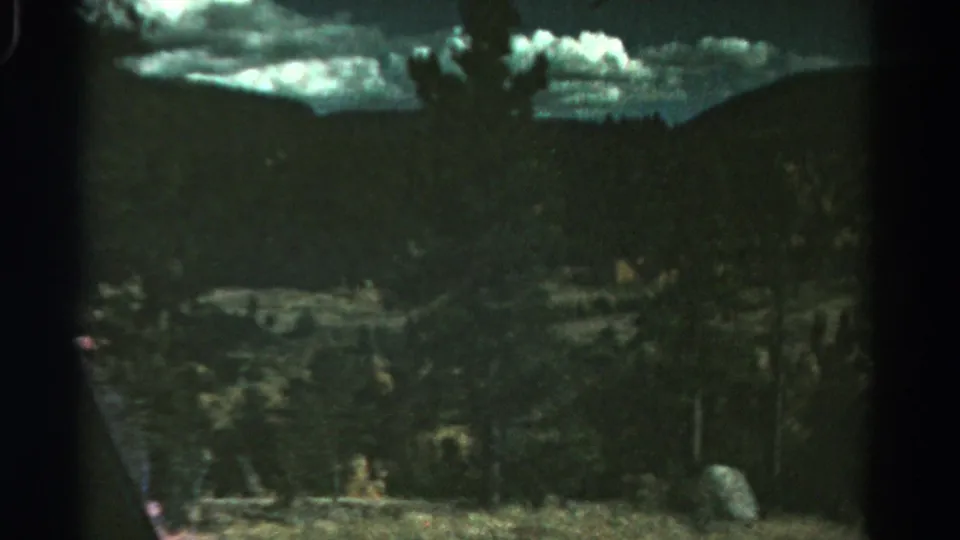1967 Colorado landscape frame with a forested slope, distant ridge, pale clouds, and visible 8mm gate edges.