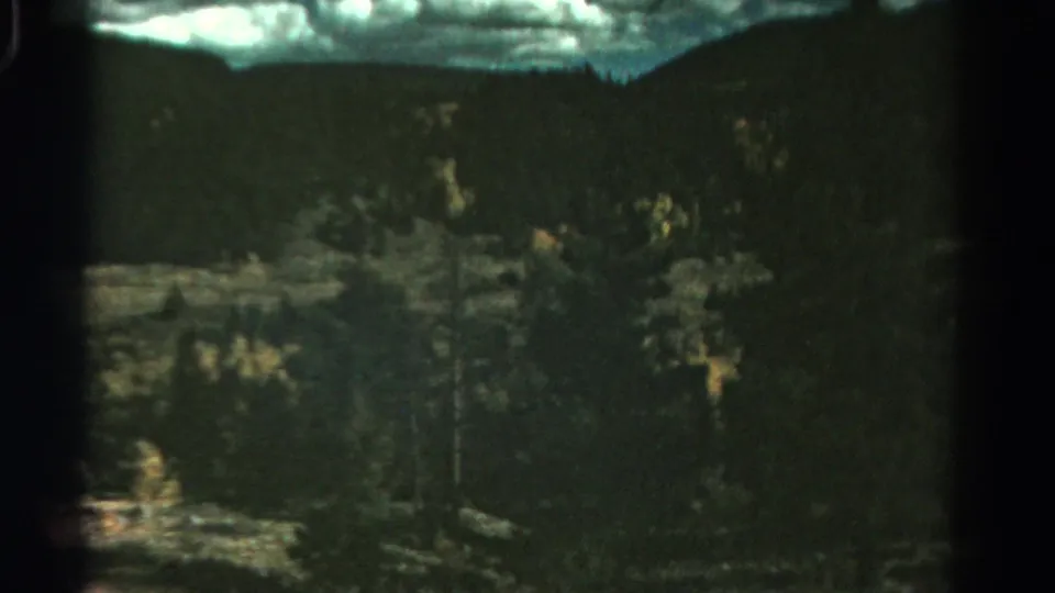 1967 Colorado 8mm frame showing a dark wooded mountain landscape with cloudy sky and small patches of autumn foliage.