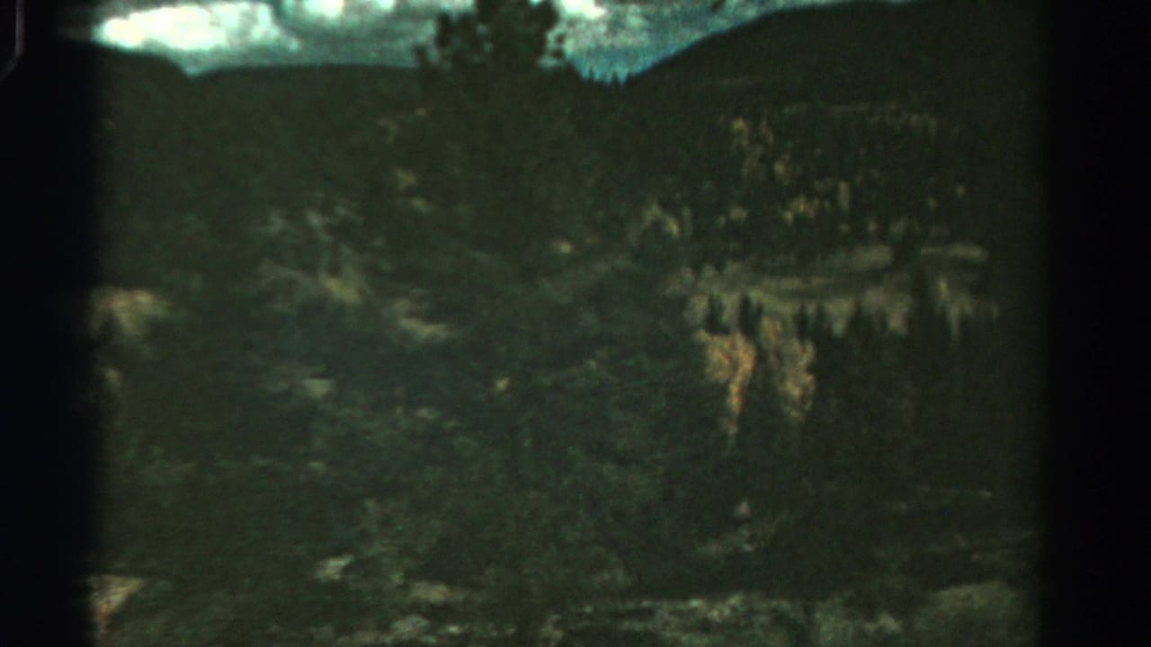 Wooded mountain terrain with muted green slopes and scattered yellow foliage.
