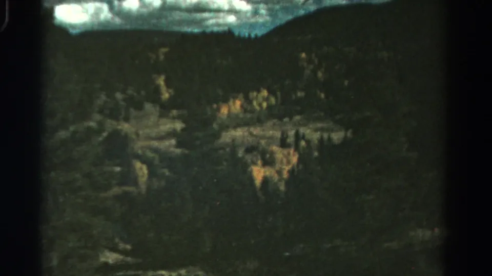 Colorado mountain landscape on 8mm film, showing dark wooded hillsides and autumn color in the midground.