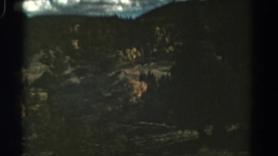 Late clip frame from a 1967 Colorado 8mm mountain view, with evergreen forest, rocky terrain, and autumn foliage patches.